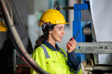 female maintenance engineer in uniform helmet safety talk by walki talkie and inspection check control heavy machine in industrial factory. technician worker check for repair factory machine