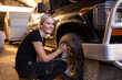 © Austockphoto - Caucasian woman fixing the tire of a classic SUV in a garage