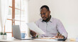 © wichayada - Portrait of handsome African black young business man working on laptop at office desk.