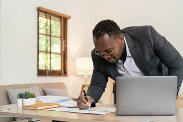 Wall Mural - Professional male economist searches needed information on portable computer, happy to recieve high net profit, spends important banking operation. Black male trader analyzes financial market.