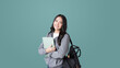 © saksit - Young Asian girl college student with tablet and backpack isolated over teal background