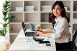 © Tj - Sharing good business news. Attractive young businesswoman talking on the mobile phone and smiling while sitting at her working place in office and looking at laptop.