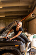 © Austockphoto - happy young female tradesperson mechanic fixing car engine in automotive repair garage