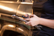 © Austockphoto - Close up shot of a woman leaning on SUV holding a mobile phone and a spanner in auto garage workshop