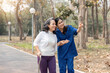 © Natee Meepian - nurse helping elderly woman with walker Nurse holding hand and help elderly woman walking in park facility