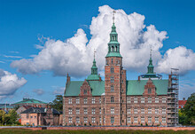 Copenhagen, Denmark - September 13, 2010: Full Rosenborg Slot West Red Stone Facade With Tower And Green Steeple Under Blue Cloudscape. Green Foliage And Scaffold On South 