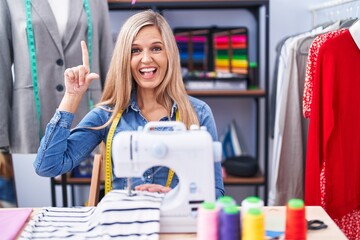 Poster - Blonde woman dressmaker designer using sew machine smiling amazed and surprised and pointing up with fingers and raised arms.