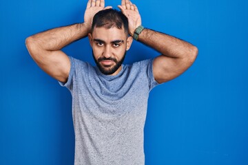 Canvas Print - Middle east man with beard standing over blue background doing bunny ears gesture with hands palms looking cynical and skeptical. easter rabbit concept.