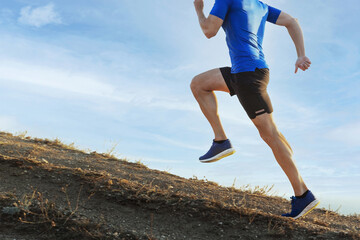 Poster - male runner run steep mountain climb on trail in blue sky background, overcoming difficulties in sports