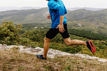 Wall Mural - male runner in windbreaker and tights running along precipice, man jogger athlete run mountain trail