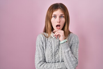 Poster - Beautiful woman standing over pink background looking fascinated with disbelief, surprise and amazed expression with hands on chin