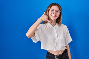 Sticker - Beautiful woman standing over blue background smiling doing phone gesture with hand and fingers like talking on the telephone. communicating concepts.