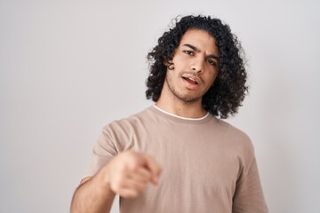 Wall Mural - Hispanic man with curly hair standing over white background pointing displeased and frustrated to the camera, angry and furious with you