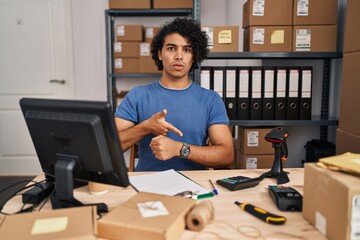 Wall Mural - Hispanic man with curly hair working at small business ecommerce in hurry pointing to watch time, impatience, upset and angry for deadline delay