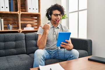 Poster - Hispanic man with curly hair doing online session at consultation office pointing thumb up to the side smiling happy with open mouth