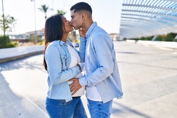 Poster - Young latin couple expecting baby touching belly and kissing at street