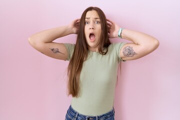 Wall Mural - Beautiful brunette woman standing over pink background crazy and scared with hands on head, afraid and surprised of shock with open mouth