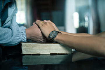 Two hands of married couple praying on the Bible in their home, faith and trust. Family, worship and praise with married couple man and woman united in prayer, holy or gratitude to Jesus Christ.