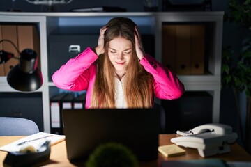 Wall Mural - Young caucasian woman working at the office at night suffering from headache desperate and stressed because pain and migraine. hands on head.