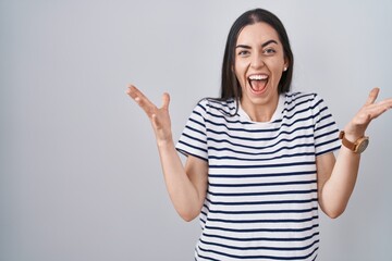 Sticker - Young brunette woman wearing striped t shirt celebrating crazy and amazed for success with arms raised and open eyes screaming excited. winner concept