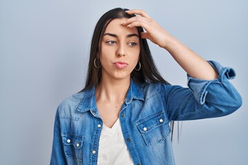 Sticker - Hispanic woman standing over blue background worried and stressed about a problem with hand on forehead, nervous and anxious for crisis