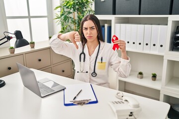 Poster - Hispanic doctor woman holding support red ribbon with angry face, negative sign showing dislike with thumbs down, rejection concept