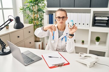 Wall Mural - Young doctor woman wearing uniform and stethoscope with angry face, negative sign showing dislike with thumbs down, rejection concept