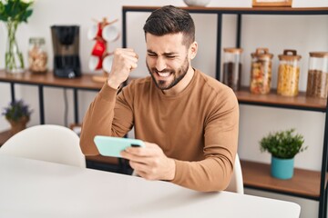 Wall Mural - Young hispanic man using smartphone sitting on table at home