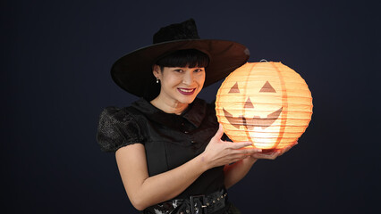 Canvas Print - Young chinese woman wearing witch costume holding halloween pumpkin lamp over isolated black background