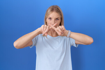 Poster - Young caucasian woman wearing casual blue t shirt rejection expression crossing fingers doing negative sign