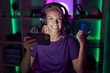 © Krakenimages.com - Young gamer woman playing video games with smartphone pointing thumb up to the side smiling happy with open mouth