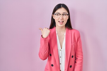 Sticker - Chinese business young woman wearing glasses smiling with happy face looking and pointing to the side with thumb up.