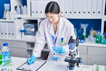 Chinese woman scientist measuring liquid writing on document at laboratory