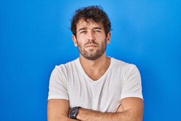 Sticker - Hispanic young man standing over blue background skeptic and nervous, disapproving expression on face with crossed arms. negative person.