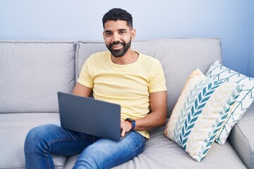 Wall Mural - Young arab man using laptop sitting on table at home