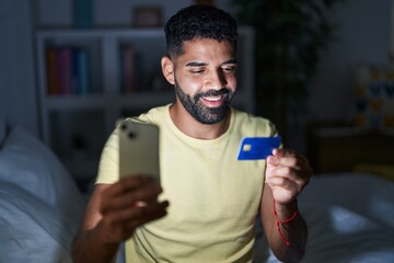 Wall Mural - Young arab man using laptop and credit card sitting on bed at bedroom