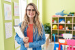 © Krakenimages.com - Young caucasian woman working as teacher at kindergarten looking positive and happy standing and smiling with a confident smile showing teeth