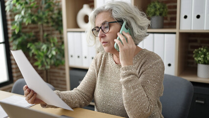 Poster - Middle age woman with grey hair business worker talking on smartphone reading document at office