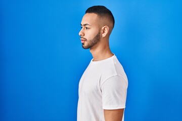 Sticker - Young hispanic man standing over blue background looking to side, relax profile pose with natural face and confident smile.