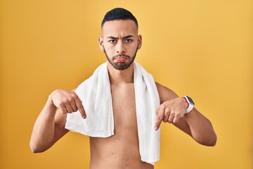 Poster - Young hispanic man standing shirtless with towel pointing down looking sad and upset, indicating direction with fingers, unhappy and depressed.