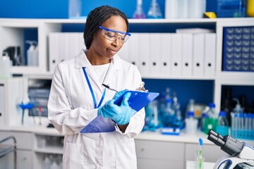 Sticker - African american woman wearing scientist uniform writing on clipboard laboratory