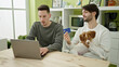Two men couple shopping with laptop and credit card sitting on table with dog at dinning room