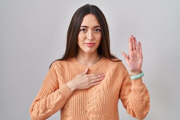 Sticker - Young brunette woman standing over white background swearing with hand on chest and open palm, making a loyalty promise oath