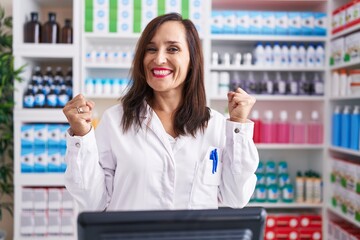 Poster - Middle age brunette woman working at pharmacy drugstore celebrating surprised and amazed for success with arms raised and open eyes. winner concept.