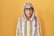 © Krakenimages.com - Middle age woman with grey hair standing over yellow background wearing glasses skeptic and nervous, frowning upset because of problem. negative person.