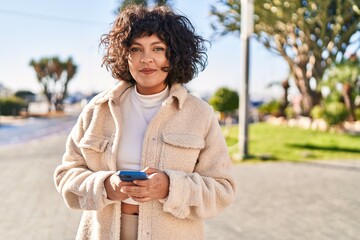 young beautiful hispanic woman smiling confident using smartphone at park