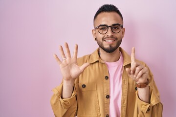 Poster - Young hispanic man standing over pink background showing and pointing up with fingers number six while smiling confident and happy.