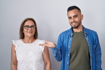 Sticker - Hispanic mother and son standing together smiling cheerful presenting and pointing with palm of hand looking at the camera.