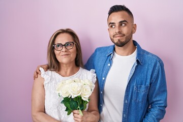 Wall Mural - Hispanic mother and son together holding bouquet of white flowers smiling looking to the side and staring away thinking.