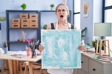 Canvas Print - Young caucasian woman holding canvas at art studio angry and mad screaming frustrated and furious, shouting with anger. rage and aggressive concept.